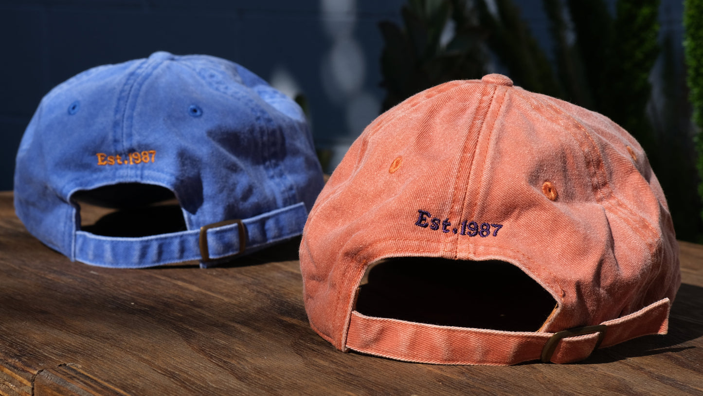 Two distressed baseball caps, one blue and one orange, on a wooden surface with a blurred natural background.
